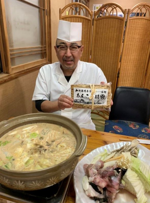 アンコウ鍋を前に、商品化した「北海道余市あんこう鍋セット」を持つ鳴海店主