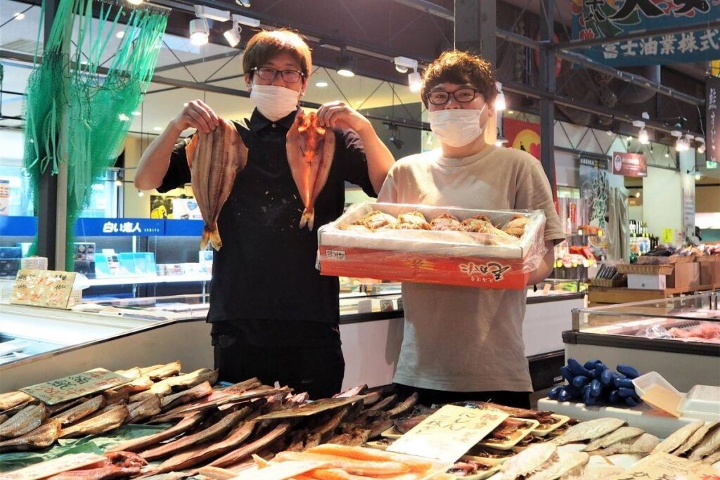 ホッケや毛ガニなど、新鮮な魚介類をすすめる２人の従業員