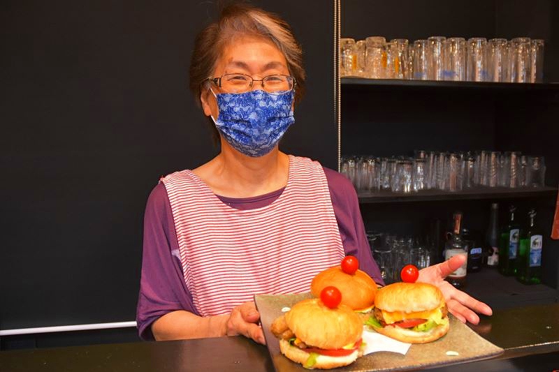 町内の居酒屋「はまなす」が提供するハンバーガーを手にする女性