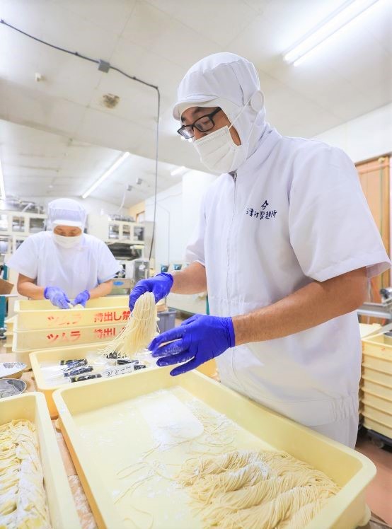 製麺工場内で手作業で麺の袋詰めをする津村健太社長