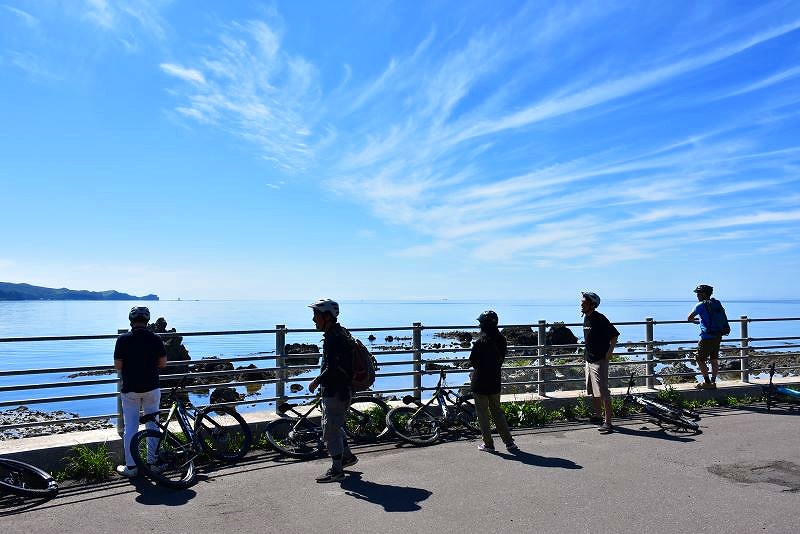 電動アシスト付き自転車「Ｅバイク」ツアーの休憩中に神威岬（左奥）の眺めを楽しむ参加者