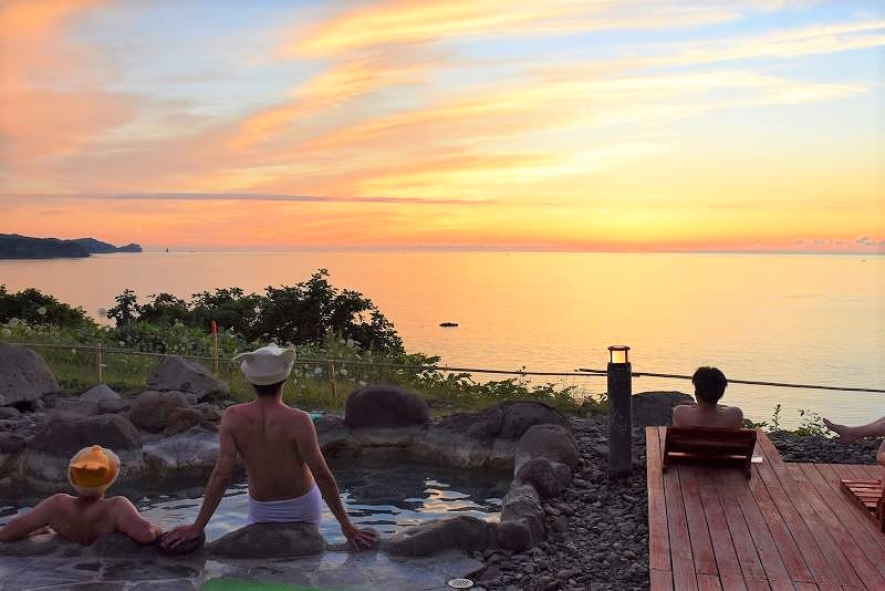 日本海に沈む夕陽が海と空をオレンジに染める「岬の湯しゃこたん」の露天風呂からの景色。