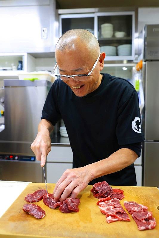 包丁を手に肉を切り分ける店主の堀口さん