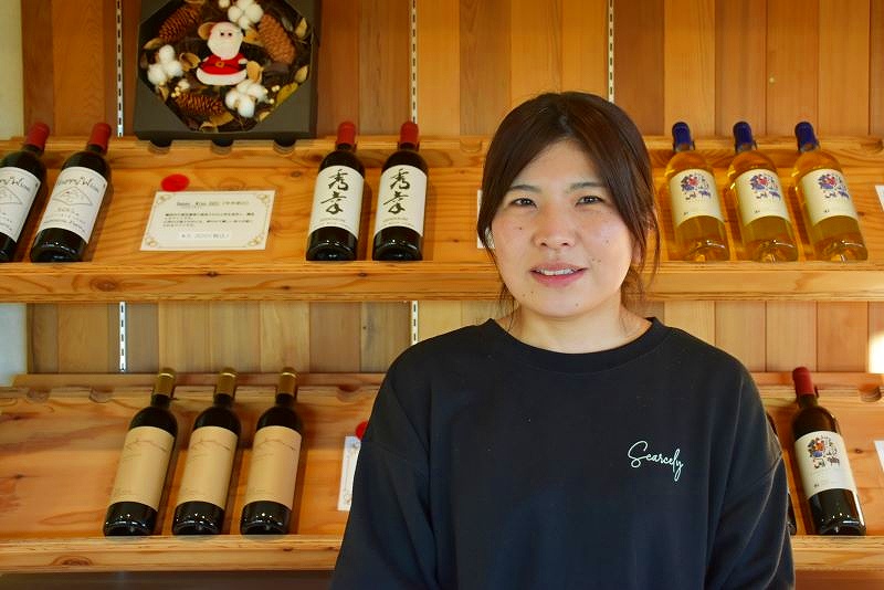 ワインボトルが並ぶ商品棚の前で笑顔を見せる醸造責任者の森裕子さん
