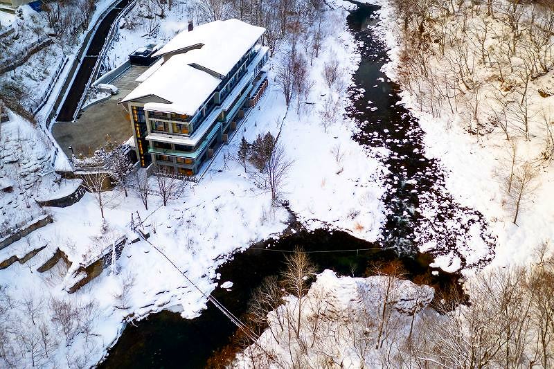 上方から俯瞰した宿泊施設「シャレーアイビー定山渓」の建物や、雪で白く染まった川など周辺の様子