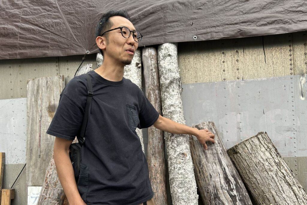 「アイスプロジェクト」の工房前で木材について説明する小助川さん