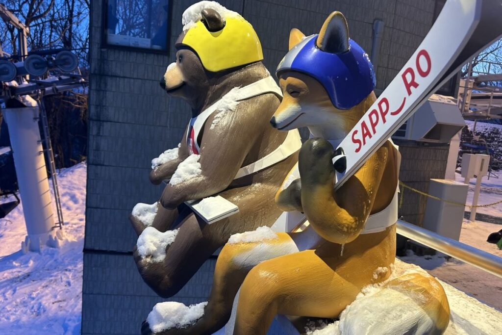 スキー板を抱えるキツネとクマ。背番号は札幌大会開催の「19」「72」