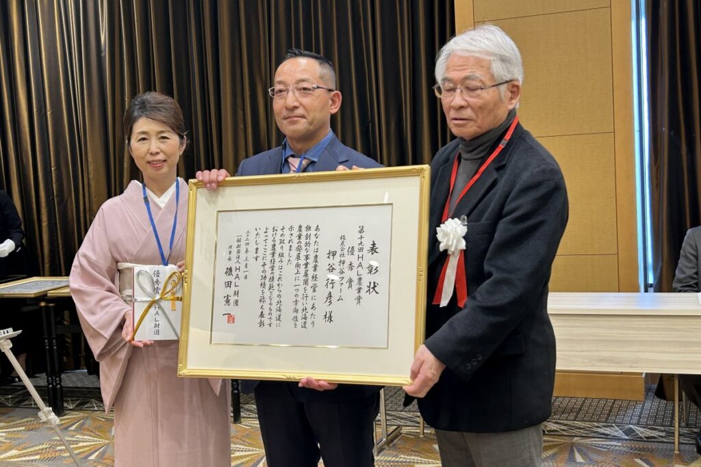 磯田理事長（右）から表彰状などを受け取った押谷さん（中央）と妻志都香さん