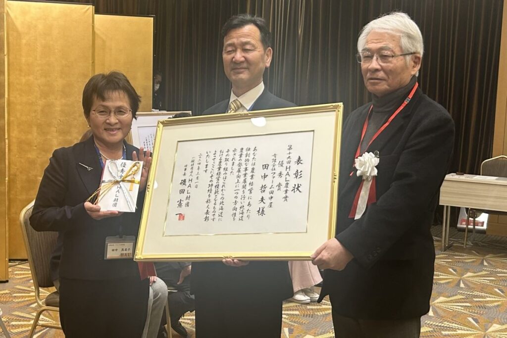 磯田理事長（右）から表彰状などを受け取った田中さん（中央）と妻真里子さん
