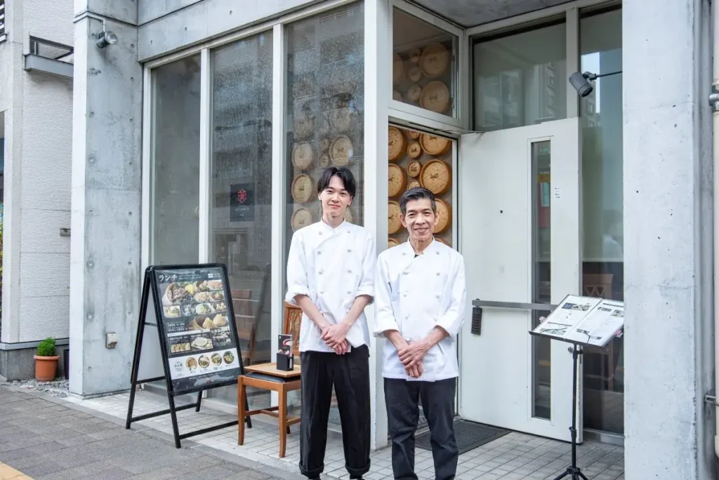 店の前に立つ、シェフのファンさん（右）と長年の相棒、料理人の中村さん（左）