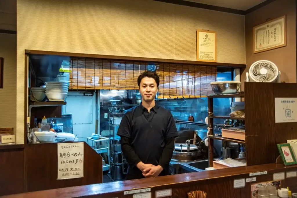 店内カウンター前に立って笑顔を見せる店主の遠藤佳輝さん