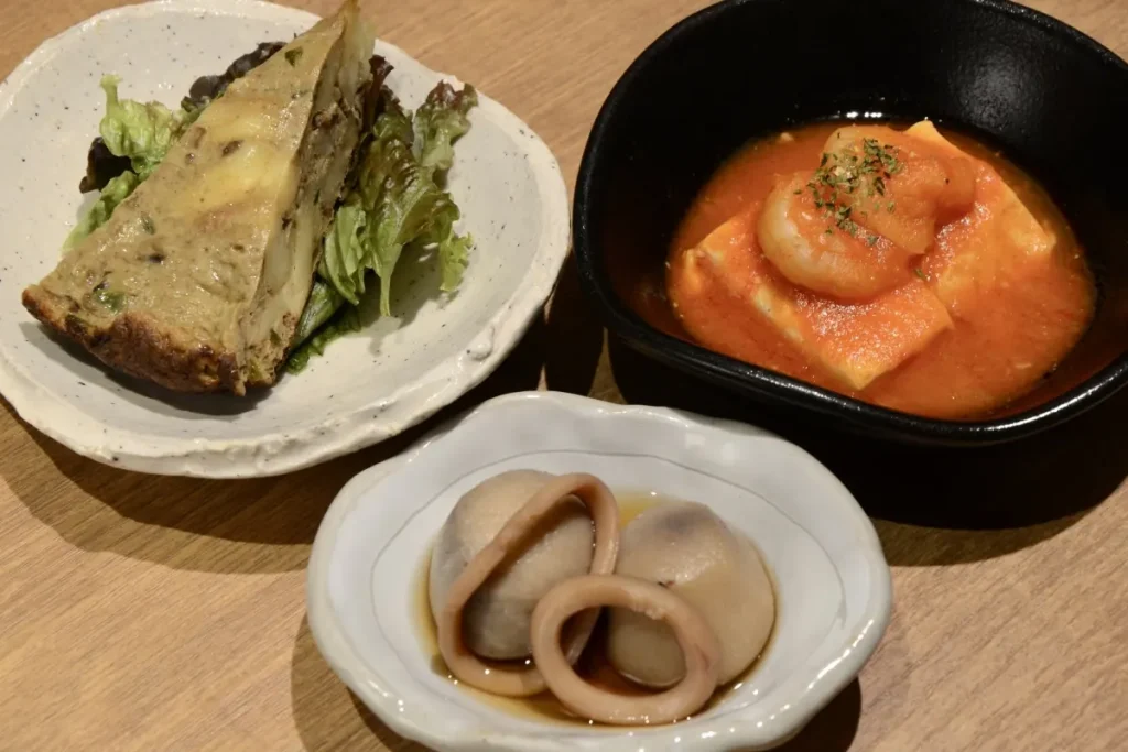  「イカと里芋煮」（手前）、「スペイン風カレーオムレツ」（左奥）、「エビチリ豆腐」の副菜３品