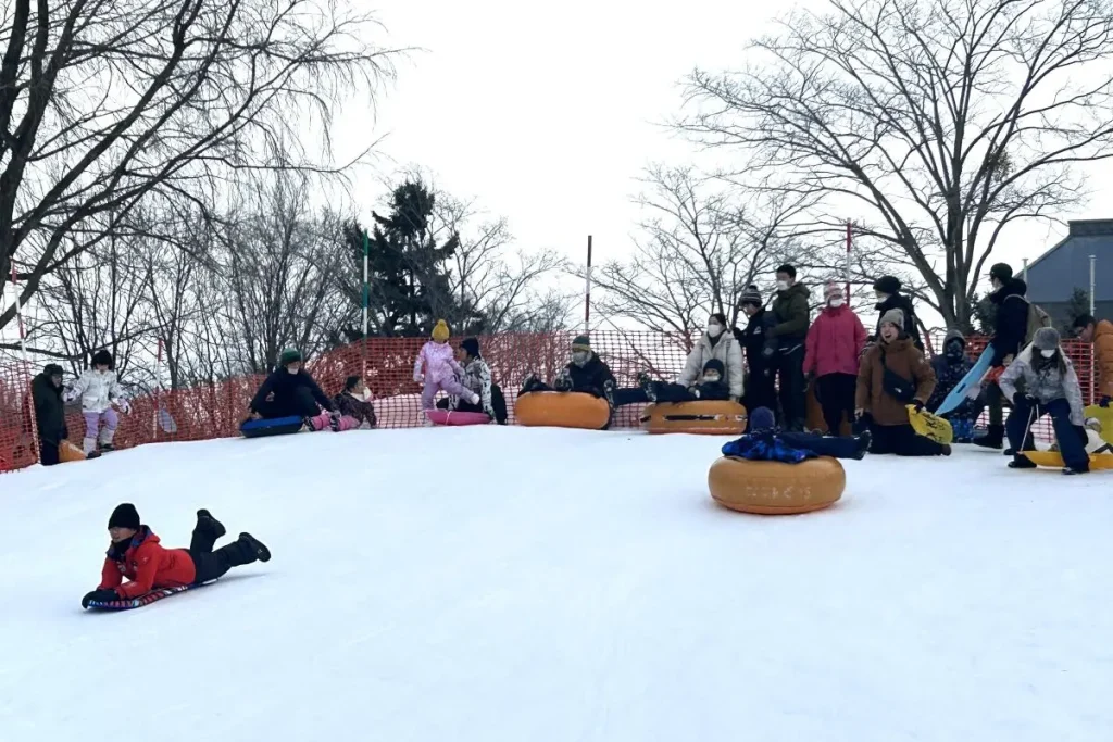 そりやチューブで雪山を滑り降りる子どもたち