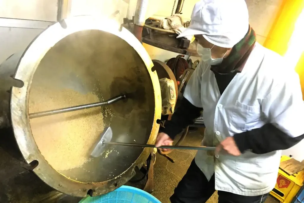 蒸し終えた大豆を蒸気釜から取り出す内藤食品工業の内藤孝幸社長(内藤食品工業提供)