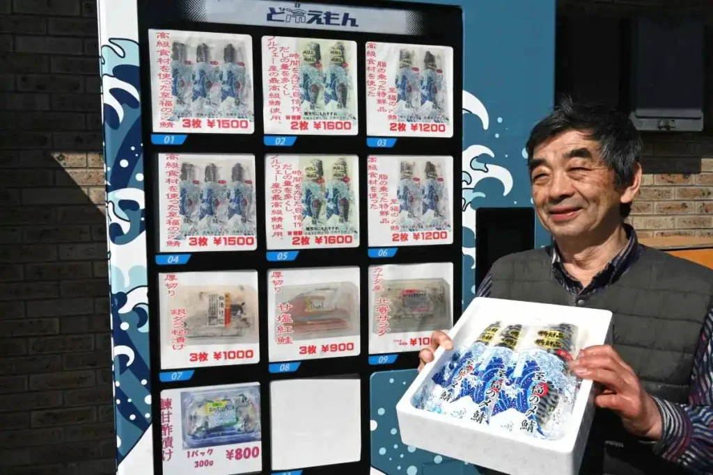 遠方の客でも買えるように設置した自動販売機。商品を手にPRする店主の高橋啓一さん