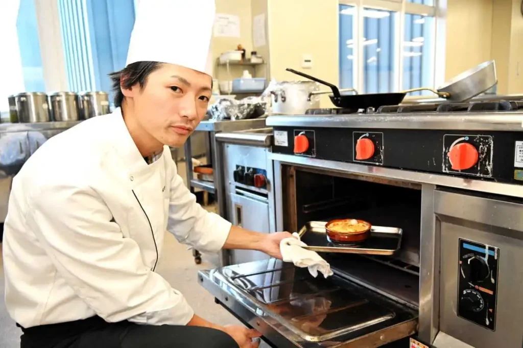 焼き上がった「タラとアサリと白カブのグラティネ」をオーブンから取り出す藤田さん