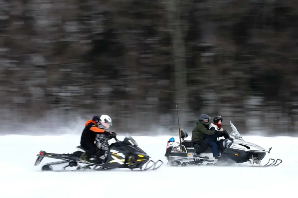 林を背に雪原を疾走するスノーモービル（星野雄飛撮影）