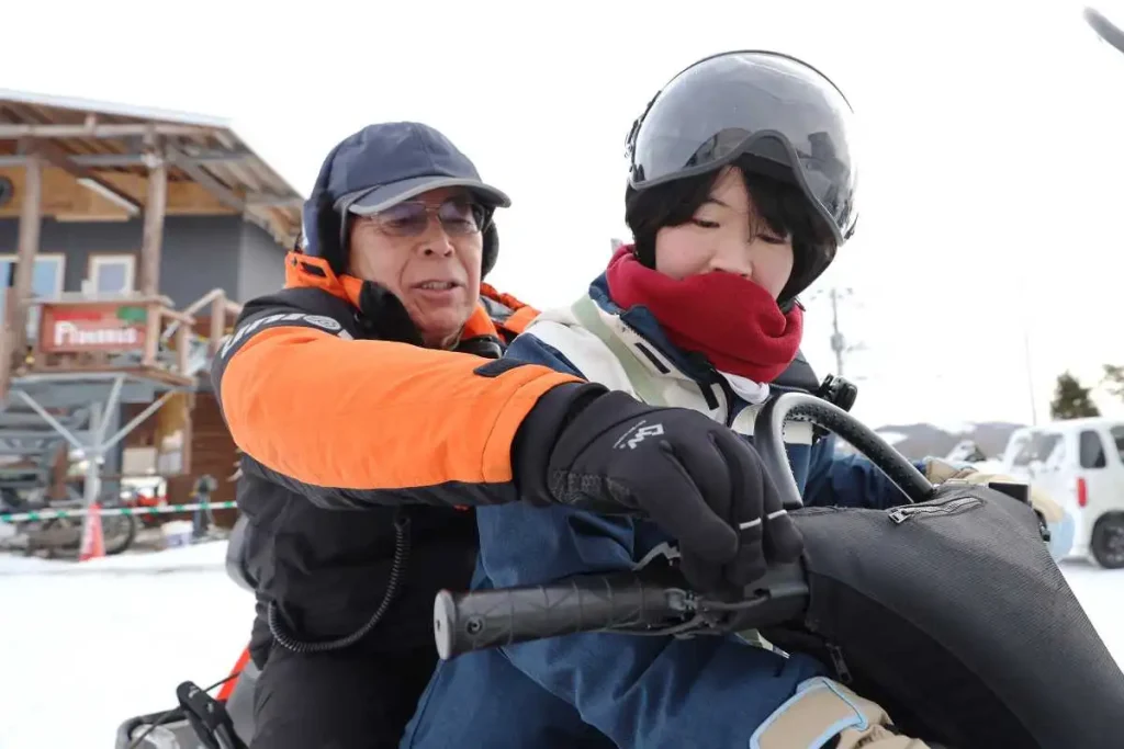 スノーモービルの運転を鈴鹿さん（左）に教わる記者（星野雄飛撮影）